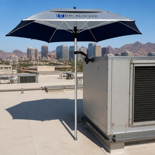 UV-Blocker ServiceShield umbrella clamp-mounted on a rooftop HVAC unit, providing shade for technicians with a city skyline and mountains in the background — occupational sun protection for HVAC and roofing work