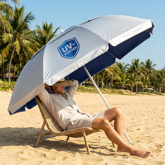 Person relaxing under a silver UV-Blocker branded umbrella on a sunny beach, demonstrating UPF 55+ sun protection